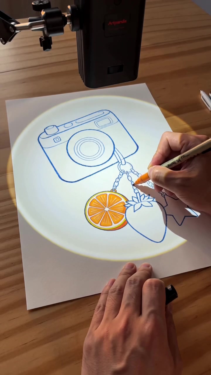 A hand coloring a camera illustration under a projected guide